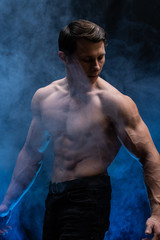 Fototapeta na wymiar Muscular man showing muscles isolated on the black background with colored smoke. Concept of healthy lifestyle 