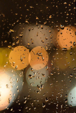 Luces desenfocadas detr&aacute;s de un cristal salpicado de gotas de lluvia