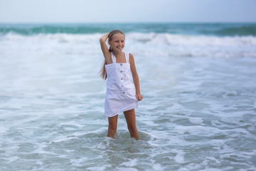 Fototapeta na wymiar Portrait of a happy Russian little girl in a white dress on a background of the sea. The child walks in the fresh air. Vacation.