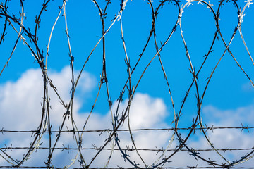 fence with barbed wire against blue sky with clouds