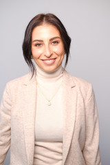 Obraz premium Portrait of a smiling mid-aged business woman in a light milk-colored trouser suit and turtleneck against a light wall.