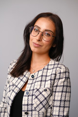 Portrait of a smiling mid-aged business woman with dark hair and brown eyes in glasses and a jacket against a light wall