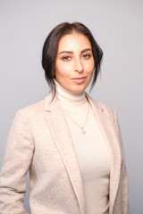 Obraz premium Portrait of a smiling mid-aged business woman in a light milk-colored trouser suit and turtleneck against a light wall.