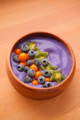 Smoothies of violet color from banana and currant, on top of a blackberry, physalis and kiwi berry. Smoothies in a wooden bowl.