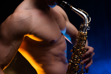Muscular man with naked torso playing on saxophone with smoked colorful background 