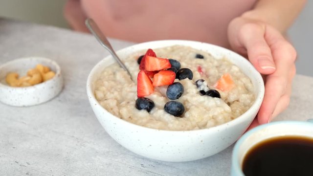 Adding berries to oatmeal porridge. Woman eating oatmeal with fresh summer berries blueberry strawberry for breakfast. Clean eating, dieting concept