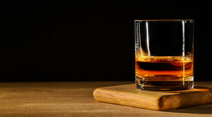 Glass with whiskey on wooden table and black background. Copy space.