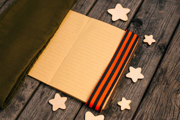 May 9. VICTORY DAY. St. George's ribbon, notebook, wooden stars, military cap. Wooden background. Victory, memory, the concept of veterans.