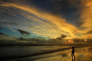 Obraz premium Silhouette boys play on the beach alone at dusk with dramatic sunset sky.