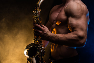 Muscular man with naked torso playing on saxophone with smoked colorful background 