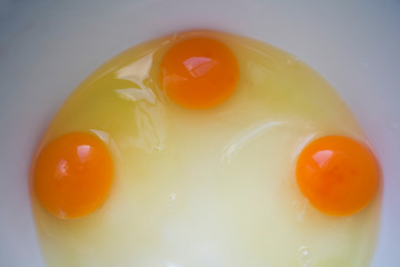 Tres huevos frescos y crudos rotos para preparar un pastel. Claras y yemas sobre fondo gris.