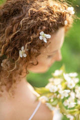 Naklejka premium Back view. A gorgeous tender girl with white flowers in curly hair holds a flowering branch in her hand. Inspiration of spring and summer. Perfume, cosmetics concept.