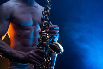 Fototapeta premium Muscular man with naked torso playing on saxophone with smoked colorful background 