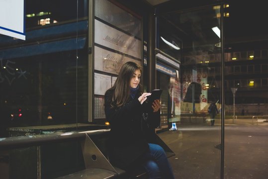 Young woman sitting bus stop using smartphone