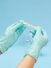 Fototapeta premium Doctor in latex gloves holding a glass mercury thermometer on blue background.