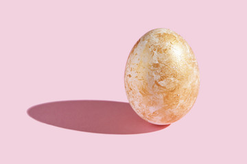 One decorative egg with hard shadow. Art easter concept. Single decorated gold color. Pink background. Horizontal
