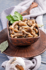 Fototapeta premium Ceramic brown bowl full of pickled honey agarics on grey napkin on grey wooden table. Fermented food. Vertical photo.