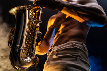 Muscular man with naked torso playing on saxophone with smoked colorful background 