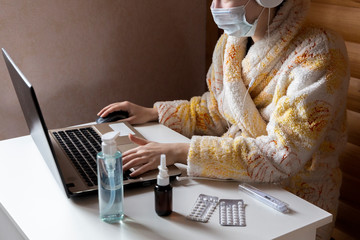 Woman with face mask working in cozy warm bath robe from home office surrounded by sanitizer, nasal...