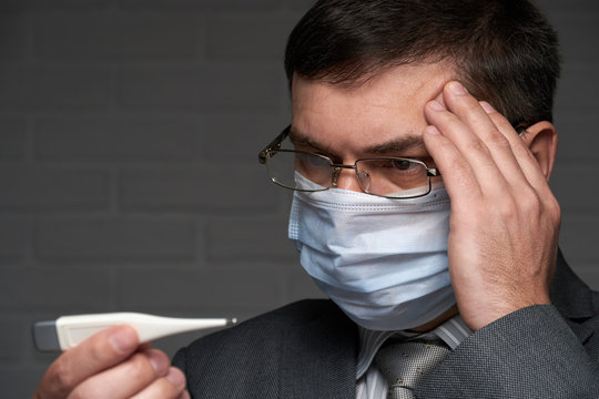 man measures body temperature with a thermometer, checks his health status, has a protective face mask - healthcare and medicine concept - Powered by Adobe
