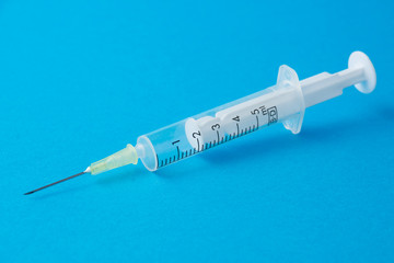 Close-up of transparent plastic syringe on blue background horizontally with copy space
