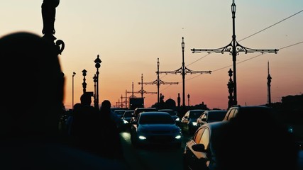 Tourists take advantage of the white nights to take a stroll across Trinity Bridge and admire the pink skies while motorvehiclists are stuck in traffic next to them. 