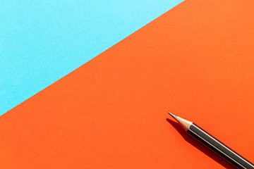 Black pencil on the blue and red and color paper texture background.