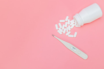 Digital thermometer and medicine pills with white bottle on pink background.
