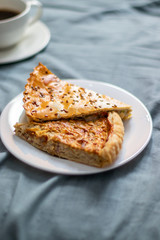 Closed piece of meat pie on a plate and cup of coffee on bed. Vertical photo