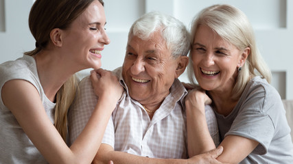 Happy older parents father and mother with adult daughter hugging close up, laughing at joke,...