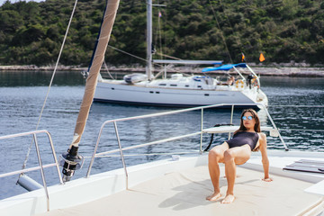 Young healthy and calm woman doing yoga on sailing yacht boat in sea at island background