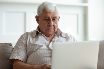 Fototapeta premium Serious older man using laptop close up, looking at screen, watching video or surfing internet, focused mature male using online clinic service or searching insurance information, medical app
