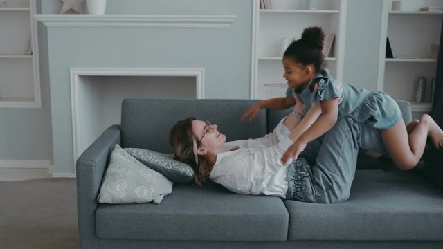 Funny kid girl having fun together fly in mothers arm practice acro pair yoga bonding friendly beautiful family, healthy young mother lifting cool child daughter up playing plane on sofa at apartment