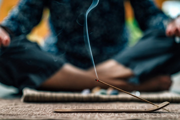 Fototapeta na wymiar Mindful Woman Meditating with Burning Incense Sticks, Sitting in Lotus Pose. Hands in Lap, Palms Facing Upwards