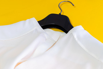 White silk classic blouse on the hanger on yellow background. Close up of detail.