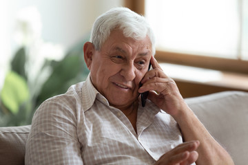 Smiling older man talking on cellphone close up, happy grandfather chatting with relatives or...