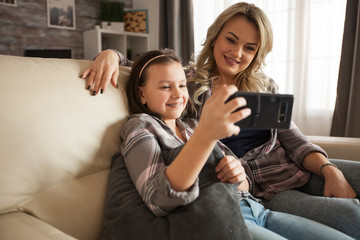 Modern mother and her little daughter watching a love video