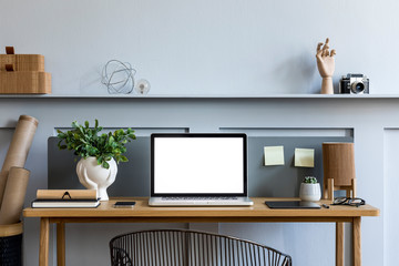 Stylish interior of home office room with mock up laptop screen, wooden desk, plant, books, notes,...