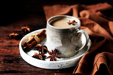 Masala tea in a ceramic mug on a dark wooden background with spices