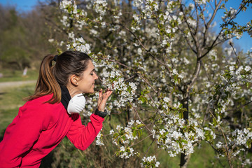 woman taking off coronavirus mask to smell blooming flowers