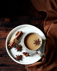 Masala tea in a ceramic mug on a dark wooden background with spices