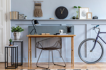 Scandinavian interior design of home office with wooden desk, modern chair, wood paneling with shelf, plant, carpet, bicycle, office supplies, marble stools and elegant personal accessories.