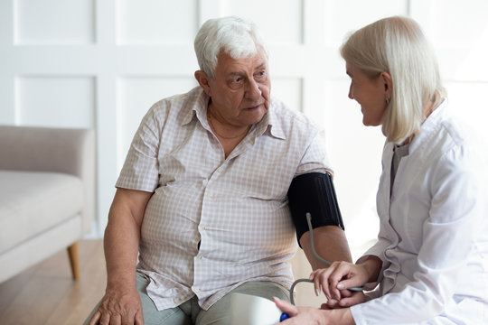 Mature doctor cardiologist wearing uniform checking older man blood pressure with tonometer during visit, checkup, middle-aged female nurse holding medical electronic device, healthcare and treatment