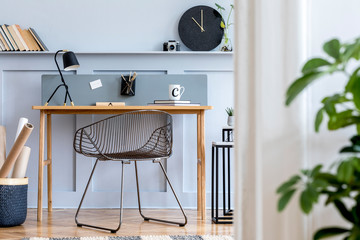 Scandinavian home office interior with wooden desk, design chair, wood panleing with shelf, plant, black clock, table lamp, office supplies and elegant accessories in modern home decor.