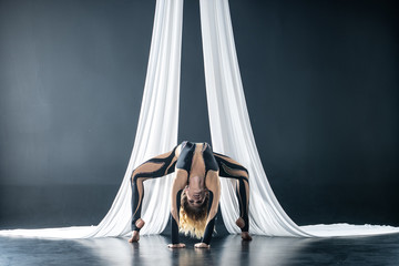 Beautiful flexible woman gymnast with white aerial silks isolated on black background
