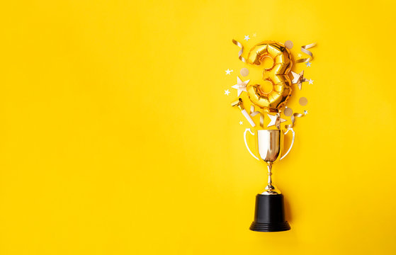 Number 3 gold anniversary celebration balloon exploding from a winning trophy