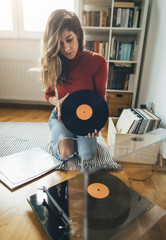 Young woman sitting on floor with vinyl record. Playing music on turntable, leisure time, hobbie
