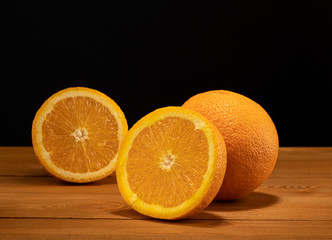 Fresh and juicy half and slice of orange fruit on a wooden table and black background.