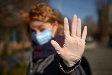 woman in a medical mask and rubber gloves raises his hand signals to stay away and keep distance