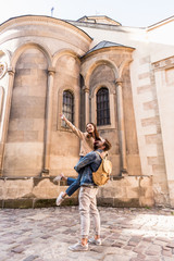 Boyfriend with backpack holding girlfriend with outstretched hand near building in city